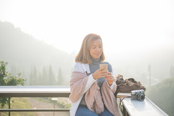 Wall Mural - Relaxed woman breathing fresh air holding coffee cup for breakfast in autumn in a forest sitting on balcony and looking at mountains and green nature.Trekking concept.