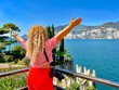 A woman with blonde curly hair enjoys views of Lake Garda in Italy. The concept of knowing the world through travel. Concept of peace and happiness.