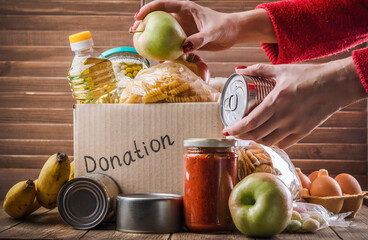 Wall Mural - Woman filling in food donation box. Pasta, cereals, various canned food in a carboard box. National food bank day or food delivery background