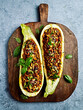 Oven baked zucchinis stuffed with minced meat, bulgur and vegetables; topped with olives, pine nuts and parmesan