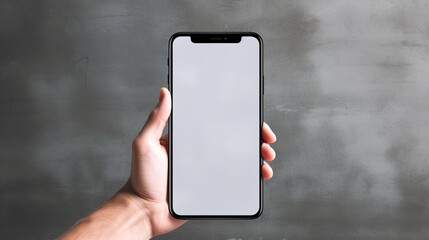 Hand holding blank mobile phone with white screen and white shoes on concrete wall. Mockup image