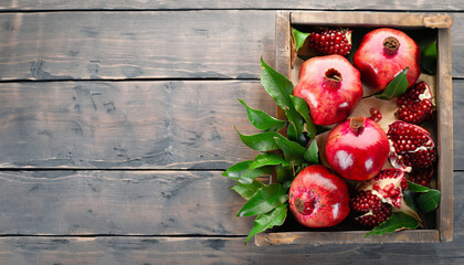 Wall Mural - Fresh pomegranates in an old box with leaves. On wooden background. Free space for text . Top view