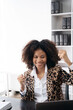 © NINENII - Overjoyed charming excited black woman business woman worker using smartphone and laptop working in office, feeling happy.