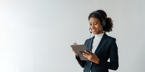 Call center operator in wireless headset talking with customer on tablet, African woman in headphones with microphone consulting client on phone in customer support service in business center