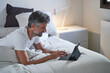 © ADDICTIVE STOCK CORE - Mature man typing on tablet keyboard while lying on bed at home