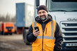 © Jasmina - Portrait of a happy smiling truck driver standing by the truck and using his phone.
