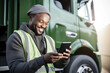 © Jasmina - Portrait of a happy smiling African american truck driver standing by the truck and using his phone.