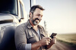 © Jasmina - Portrait of a happy smiling truck driver standing by the truck and using his phone.