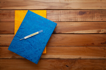 Two handmade paper Diaries, with a Thermometer on the top. Wooden background. Top view.