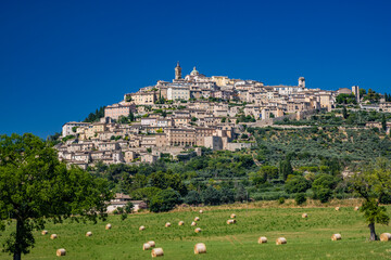 Wall Mural - Panoramic view of the beautiful village of Trevi, in the province of Perugia, Umbria, Italy. The ancient stone houses of the city, perched on the hill. A field with freshly harvested hay bales.