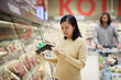 © Johnér - Woman doing shopping in supermarket and using cell phone to compare prices or checking shopping list