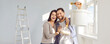 © Studio Romantic - Cheerful young family couple doing renovations at home. Joyful man and woman painting walls in their house. Banner with portrait of happy, smiling, hugging husband and wife holding bucket and roller