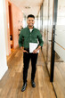 © Vadim Pastuh - Full length portrait of smiling indian businessman standing in office hallway, carrying laptop and looks at the camera. Proud and successful small business owner, freelancer guy in coworking space