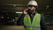 © Yuliia - Professional industrial manufacture business industry worker Arabian bearded engineer Indian man in glasses builder in safety uniform hard hat talking phone speak smartphone at parking lot at factory