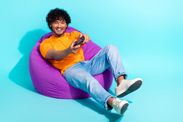 Full size photo of positive overjoyed person sit comfort bag hold controller play video games isolated on teal color background