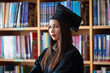 © EduLife Photos - Portrait young happy and excited Asian woman university graduate in graduation gown and cap in the library. Education stock photo