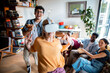 © Marko Geber - Young and diverse group of friends using a vr headset to play games together in the living room of their flatshare apartment