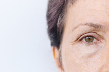 Close up of an elderly caucasian woman's face with puffiness under her eyes and facial wrinkles isolated on a white background. Age-related skin changes, fatigue. Cosmetology and beauty concept