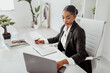 Professional recruitment concept. Black female HR manager using laptop, holding candidate's CV resume, office interior
