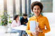 © Prostock-studio - Portrait of happy black lady university student posing with notepads while classmates studying on background in audience
