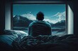 Young man sitting in bed looking at the mountains through the window