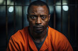 © Sergio - African American prisoner in prison, portrait of sad adult man in an orange robe sitting in prison cell. Crime, arrest