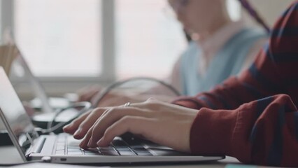 Closeup of unrecognizable hands of schoolboy typing on laptop keyboard during programming lesson in class