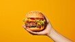Hands holding a burger yellow background