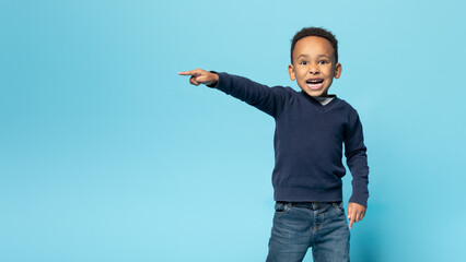 Wall Mural - Funny african american boy pointing aside at copy space, emotional male child demonstrating free place for ad