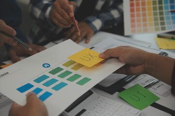 Close up ux developer and ui designer brainstorming about mobile app interface wireframe design on table with customer breif and color code at modern office.Creative digital development agency