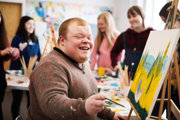 Young smiling man with Down syndrome on art workshop with a group of students, learning a new skill. Social integration concept.