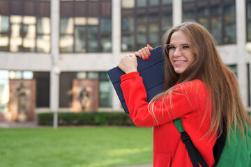 Wall Mural - young college or university student, happy girl outdoors at campus in glasses with braces. Portrait of teen, female teenager in red hood with tablet computer.