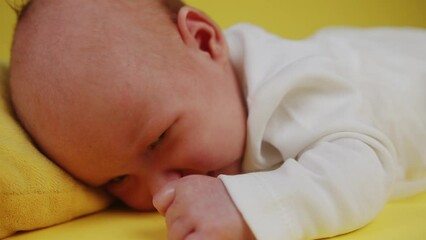 capricious baby licking fist on yellow background. close up.