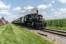 Strasburg, Pennsylvania – August 2023: Strasburg Steam Train Rides Along Though Corn Fields In Lancaster County, Pennsylvania