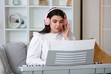 Young female musician with headphones playing synthesizer at home