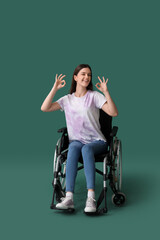 Wall Mural - Young woman in wheelchair showing OK on green background