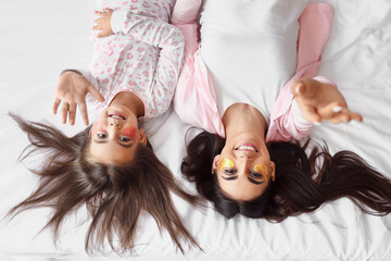 Poster - Happy mother and her little daughter with under-eye patches lying on bed, top view