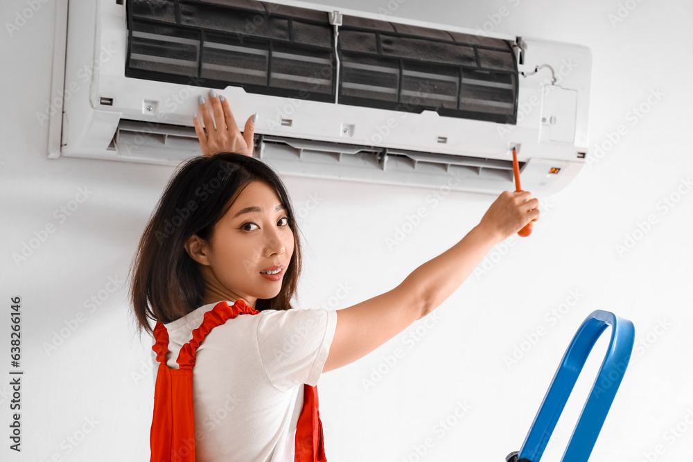 Female technician fixing air conditioner in room