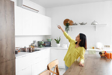 Beautiful Asian Woman Switching On Air Conditioner In Kitchen