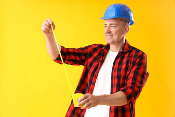 Wall Mural - Mature worker with tape measure on yellow background. Labor Day celebration