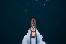 Top View Of A Wooden Powerful Motor Boat. Luxurious Wooden Boat Fast Movement On Dark Water.Man And Woman In Luxury Expensive Wooden Speedboat Fast Moving On Dark Water Top View.