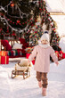 Little girl in winter clothes on standing cheerful on a decorated Christmas street in winter concept of Christmas or New Year greetings