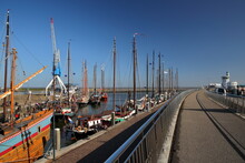 The Walking Path Leading To The Main Harbor And The Railway Station In Harlingen, Friesland, Netherlands, With Old Wooden Sailing Boats Mooring And Harbor Cranes On The Left