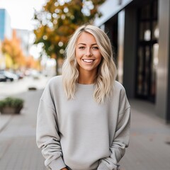 Beautiful young lady dressed in gray sweater, commercial sweatshirt mock-up, smiling blonde woman standing in the street