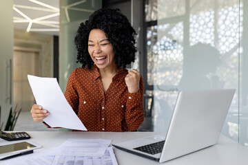 Successful financier woman satisfied with results ,checking report businesswoman at workplace, happy holding hand up triumphant winner gesture african american boss behind paper work with notebook