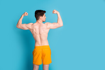 Poster - Photo portrait of attractive young man raise fists flex muscles show back dressed stylish yellow shorts isolated on blue color background