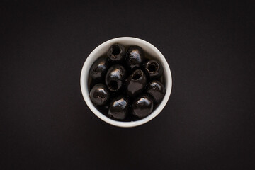 Wall Mural - Black olives in a white bowl on a black background
