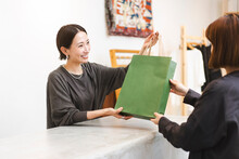 働く日本人女性/アパレル店員/お買い上げ商品をお客様に手渡している