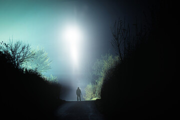 Wall Mural - A mysterious scary UFO above a hooded figure. On a spooky country road. On a foggy winters night.