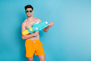 Wall Mural - Photo portrait of attractive young man hold water gun toy have fun dressed stylish yellow shorts isolated on blue color background